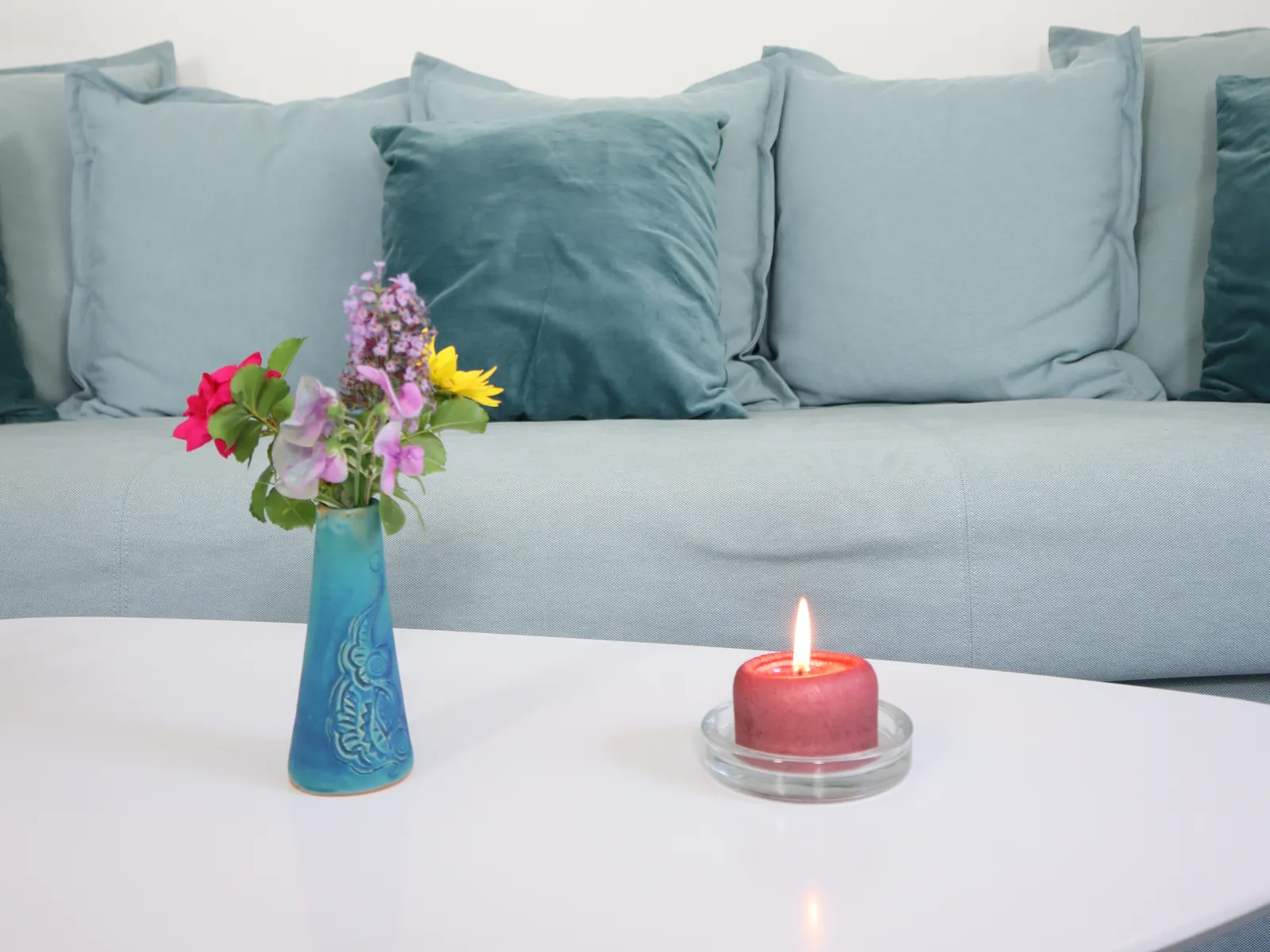Sofa mit blauen Kissen, Blumenvase und Kerze in der Praxis